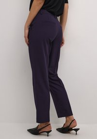 Pantalons taillés violets avec une coupe slim, en tissu lisse, avec des poches latérales et des poches passepoilées à l'arrière, assortis de chaussures à bride arrière noires.