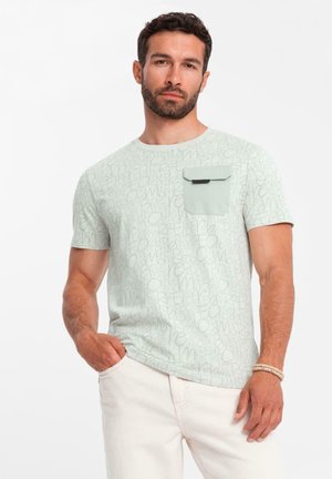 Camiseta de manga corta verde claro con texto repetido en un tono más claro, y un bolsillo contrastante en el lado izquierdo del pecho en un sólido verde más oscuro.