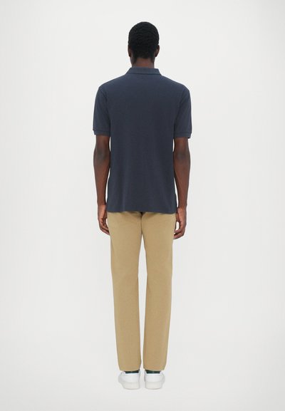 Ναυτικό πόλο μπλουζάκι με κοντά μανίκια, ελαφρώς καμπυλωτό στρίφωμα; σε συνδυασμό με μπεζ παντελόνια και λευκά αθλητικά παπούτσια; λεία υφή υφάσματος.