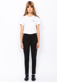 Witte short-sleeve t-shirt met klein logo, gecombineerd met zwarte broek met zijzakken. Model draagt zwarte sneakers.