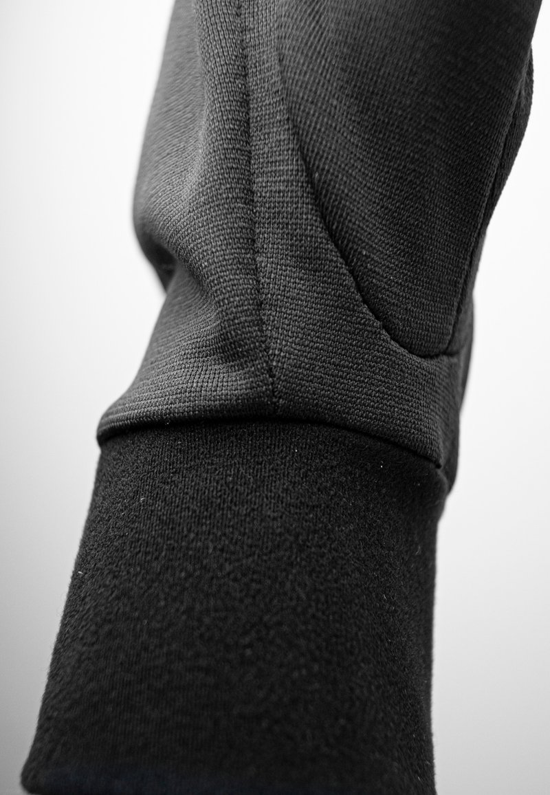 Primo piano di un tessuto nero texturizzato con una cucitura e un dettaglio di polsino visibili, che mette in mostra il materiale a maglia e le cuciture.