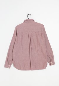 Camisa de manga larga en tejido rosa desgastado. Cuenta con un cuello, pliegue en la parte posterior y puños abotonados. Textura suave con un ajuste relajado.