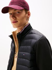 Svart puffer vest med høy krage og rød, hvit og blå detaljer, brukt over en beige genser og parret med en maroon kaps.