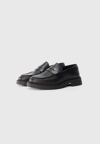Schwarze Lederl loafers mit runder Zehenpartie, ausgestattet mit Doppelstich und einer leicht erhöhten Sohle. Akzente in Rot, Weiß und Blau nahe der Ferse.