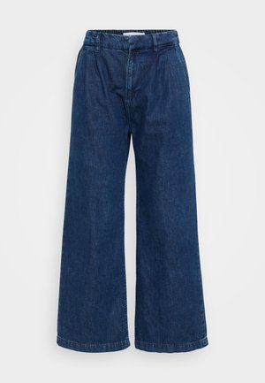 Široke traper hlače v temno modri barvi. Imajo elastičen pas, ohlapen kroj in minimalne šive na robovih.