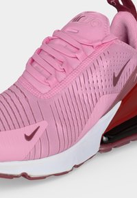 Κοντινή λήψη ενός ροζ sneaker Nike Air Max 270 με πλεκτό επάνω μέρος, ορατή μονάδα αέρα στη σόλα σε κόκκινο χρώμα και λογότυπα Nike Swoosh σε μπορντό.