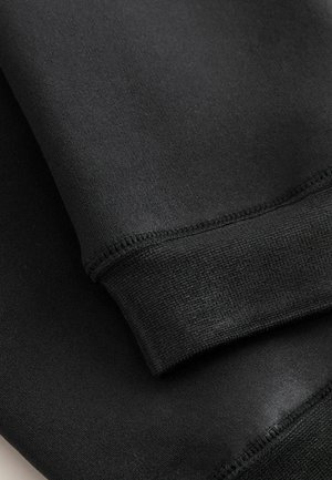 Melna auduma ar gludu tekstūru, ar elastīgu aproci ar ribotu rakstu. Šuvju līnijas redzamas gar malām, uzsverot kvalitatīvu izpildījumu.