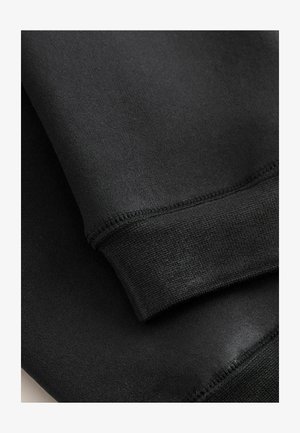 Crni materijal, glatke teksture, s rastezljivim manžetom u rebrastom uzorku. Šavovi su vidljivi duž rubova, što pokazuje kvalitetnu izradu.