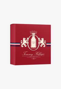 Caja de perfume roja con gráficos de león blanco, que presenta una ilustración central de la botella, una etiqueta de "Tommy Girl" y acentos a rayas azules y blancas.