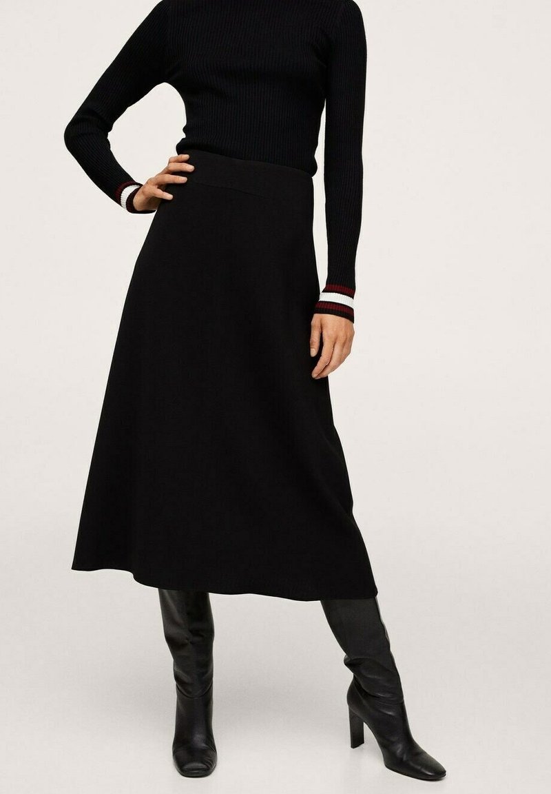 Jupe évasée noire en tissu lisse, avec un design taille haute. Associée à un pull à col roulé noir en côtes, avec des accents rayés rouge et blanc.