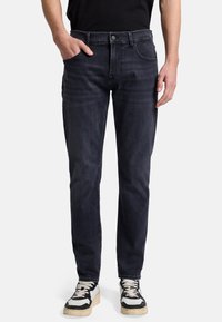 Dunkelblaue Denim-Jeans mit geradem Schnitt, Fünf-Taschen-Design, subtilen Waschungen und Kontrastnähten. Getragen mit Schwarz-Weiß-Sneakern.