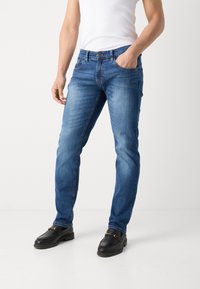 Blå denimjeans med rett snitt, fem lommer, front knappestengning og subtil falming. Kombinert med svarte slip-on sko.