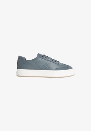 Niski szary skórzany sneaker z białą grubą podeszwą, z przodu sznurowany i wytłoczonym logo "CK" po boku.