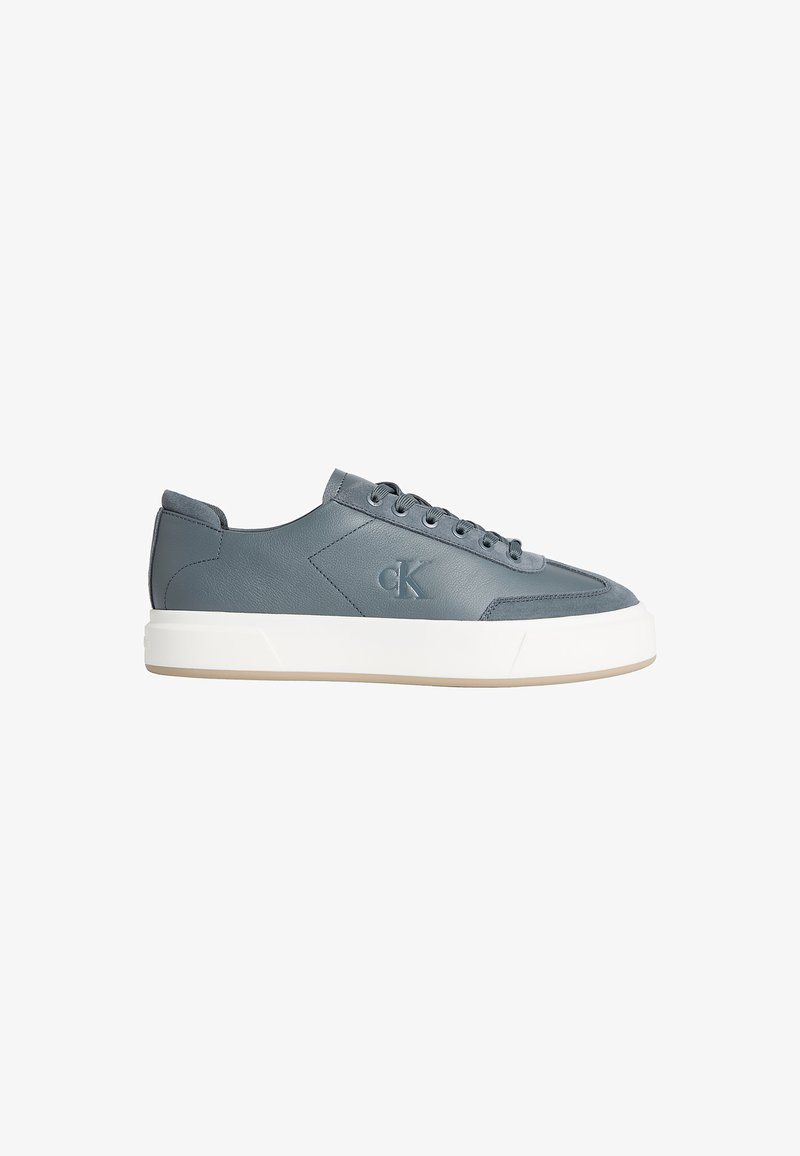 Baskets basses en cuir gris avec semelle blanche épaisse, lacets à l’avant et logo "CK" embossé sur le côté.