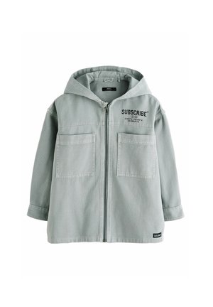Lichtgrijze gewatteerde jas met capuchon, voorzien van een ritssluiting aan de voorkant, twee grote borstzakken en zwarte tekst "SUB5CRIBE" aan de linker bovenzijde.