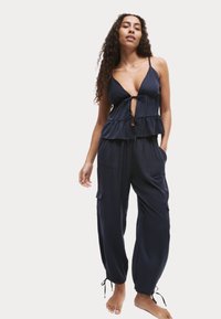 Conjunto de dos piezas en azul marino que incluye una blusa con volantes, escote en V profundo y detalles con lazo, combinada con pantalones holgados y acampanados con bolsillos laterales.