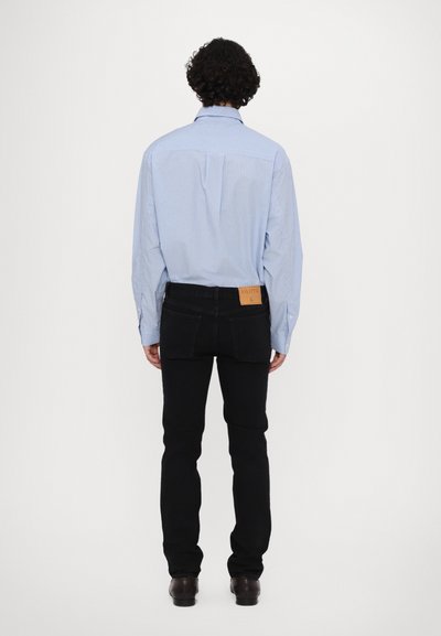 Heled sinise triibuga särgi kombinatsioon mustade teksadega, mis näitab voolujoonelist sobivust. Vöökoht on märkimisväärne nahkkleeps brändi nimega.