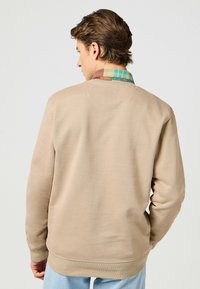 Felpa beige con vestibilità over, caratterizzata da un colletto a quadri testurizzato nei toni del blu e dell'arancio, e polsini e orlo a coste.
