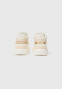 Sneaker bianchi e beige con un design massiccio, texture liscia e dettagli lucidi; presenta un logo impresso sul tallone.