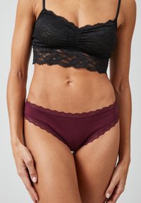 Zwarte kant bralette met een gegolfde rand, gecombineerd met bordeauxrode slipjes met kant. De stof is zacht en licht doorzichtig.