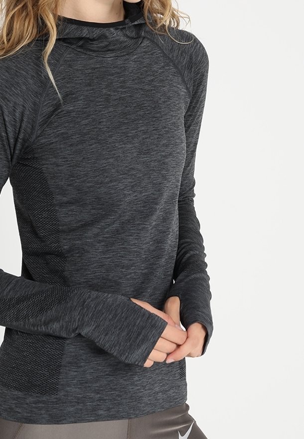 Femme portant un haut de sport à manches longues gris foncé avec des trous pour les pouces, se tenant les mains jointes, coupée au niveau du cou et des hanches.