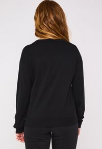 Maglione nero con maniche lunghe e polsini a coste, caratterizzato da un collo rotondo e una vestibilità rilassata. Tessuto morbido e design semplice.