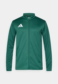 Πράσινο μπουφάν με φερμουάρ από λείο ύφασμα, διαθέτει ψηλό γιακά και λευκό λογότυπο Adidas στο αριστερό στήθος. Περιλαμβάνονται δύο πλαϊνές τσέπες.