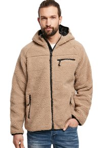 Chaqueta de forro polar beige con capucha, cierre de cremallera frontal, detalles en negro, tejido texturizado, dos bolsillos laterales y un bolsillo en el pecho.