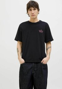 Sort bomulds t-shirt med korte ærmer, udsmykket med en lille lyserød grafisk tekst på brystet og en afslappet pasform, parret med mørke denim bukser.