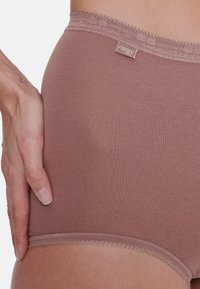 Culotte hipster pour femmes couleur marron clair avec une texture douce, taille élastique et bords décoratifs festonnés. Étiquette de marque visible sur la taille.