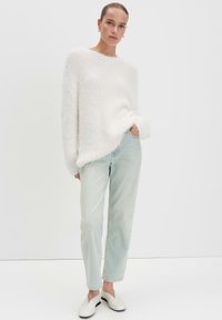Fluffy witte trui met een losse pasvorm, lichtblauwe rechte jeans en witte instappers met zwarte accenten. Eenvoudige, zachte textuur.