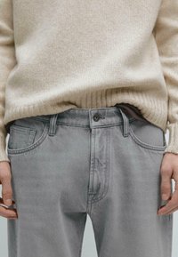 Light gray denim jeans with a smooth texture, five-pocket design, and a button fly, worn with a soft beige ribbed sweater.