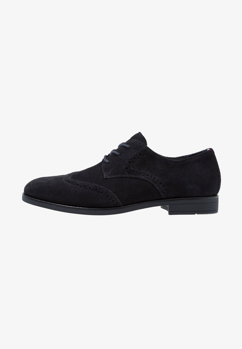 Chaussure oxford en daim noir à lacets avec perforations décoratives et petit talon, présentée de profil sur fond blanc.
