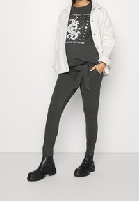 Grå grafisk t-shirt med blommönster, bärs under en ljus oversized jacka. Mörkgrå sweatpants med knytväska och svarta chunky boots.
