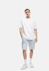 Camiseta de algodón blanca de manga corta combinada con pantalones cortos de carga de denim en un tono azul claro, que cuentan con bolsillos laterales y un corte relajado. Zapatillas blancas y calcetines.