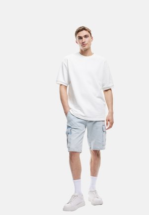 Hvid bomulds t-shirt med korte ærmer, parret med lyseblå denim cargo shorts, der har sidelommer og en afslappet pasform. Hvide sneakers og sokker.
