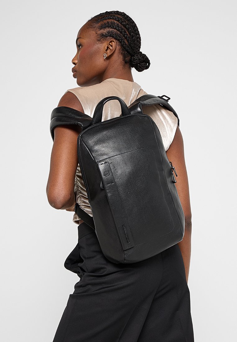 Zwarte leren rugzak met een rechthoekige vorm, gestructureerd oppervlak en bovenhandvat. Voorzien van verstelbare schouderbanden en een ritsvak.