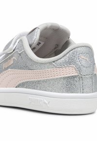 Baskets scintillantes argentées avec des accents roses, semelle blanche plate, col rembourré et détail de sangle ajustable. Logo Puma sur le côté.