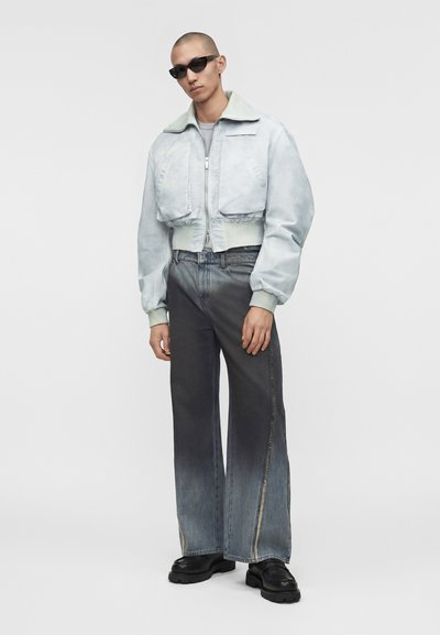 Άτομο που φοράει ανοιχτό γκρι κομμένο bomber μπουφάν, ξεθωριασμένο παντελόνι τζιν με φαρδιά μπατζάκια και πλευρικές ραφές, μαύρα χοντρά παπούτσια και μαύρα γυαλιά ηλίου.