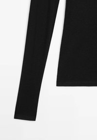 Maglietta nera a maniche lunghe realizzata in tessuto morbido. Presenta un design aderente con scollatura rotonda e polsini a coste. Colore semplice e solido.