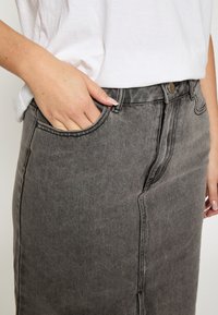 Sivá denimová sukňa s vysokým pásom, bočným vreckom a jemnými švami. Materiál vyzerá textúrovane s klasickým strihom.