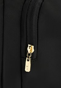 Czarna torba z tkaniny z złotym zamkiem błyskawicznym, wyposażona w szczegółowy uchwyt oraz teksturowaną powierzchnię, podkreślająca jej elegancki, nowoczesny design.