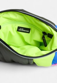 Intérieur d'un sac en tissu noir et moelleux avec une doublure vert néon vif, une poche zippée et une étiquette portant la mention "CLIO GOLDBRENNER."