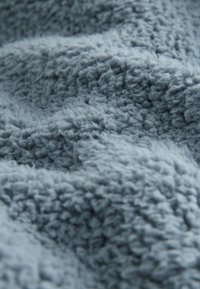 Tissu polaire bleu clair doux et texturé avec un aspect duveteux et laineux ainsi que des plis visibles créant une surface chaleureuse.