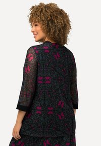 Blusa nera trasparente con un motivo floreale nei toni di rosa e blu, dotata di maniche a tre quarti e scollatura rotonda.