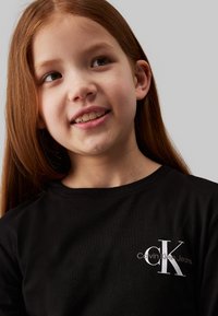 T-shirt de algodão preta com decote redondo, apresentando um logotipo branco "CK" e o texto "Calvin Klein Jeans" na área do lado esquerdo do peito.