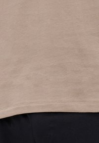 T-shirt en coton beige avec une texture douce, présentant un ourlet arrondi, des manches courtes et des détails de couture subtils.