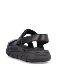 Sandales noires avec un design de sangle texturé, fermeture ajustable en Velcro et une semelle épaisse et contourée pour le confort et le soutien.