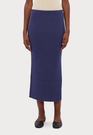 Ribbed knit midi skirt in deep navy, featuring a fitted silhouette and subtle hem slit. Paired with black flat shoes.