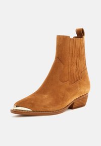Botine din suede crem cu vârf ascuțit și capac metalic aurie. Dispune de panouri laterale elastice și un toc mic, căptușit. Suprafață texturată.